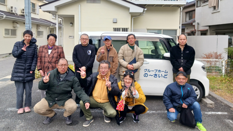施設の利用者と職員が施設の車の前で集合写真を撮影している様子